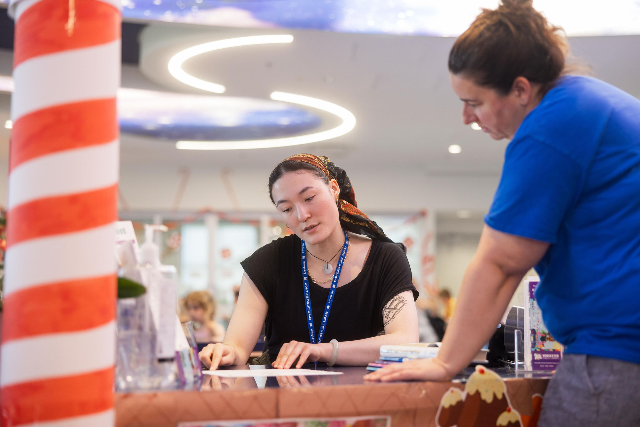 A librarian helps a patron at a service desk.