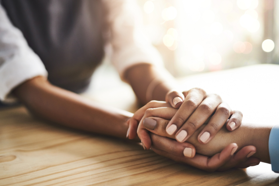 Picture of someone holding another person's hand to comfort them, points to Community Resources page.