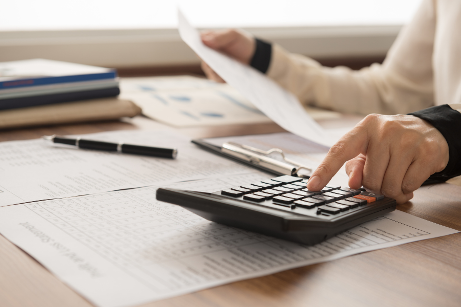 A person works on financial papers using a calculator.
