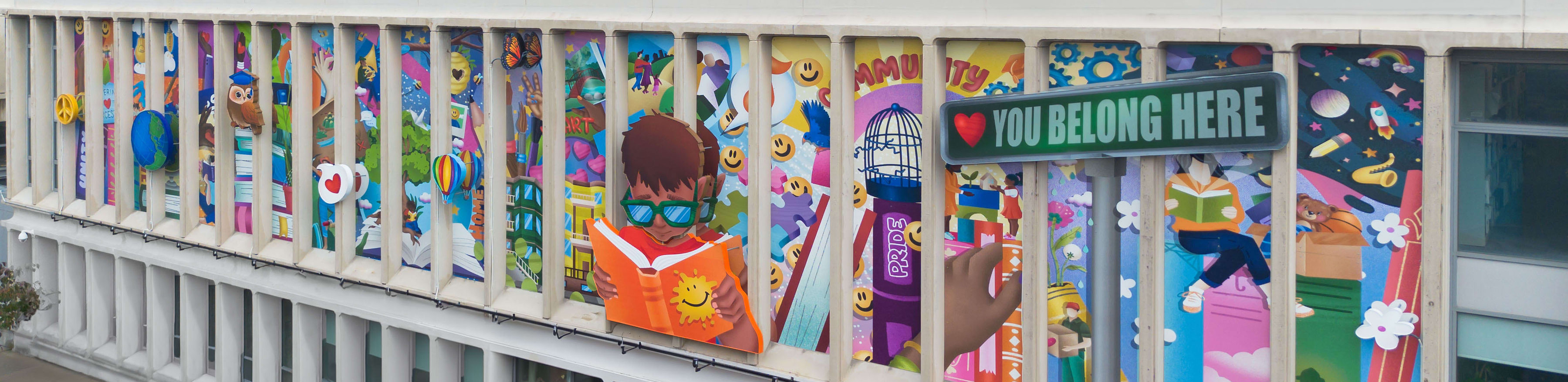 An outdoor sign at the Worcester Public Library features a boy reading surrounded by lots of colorful elements.