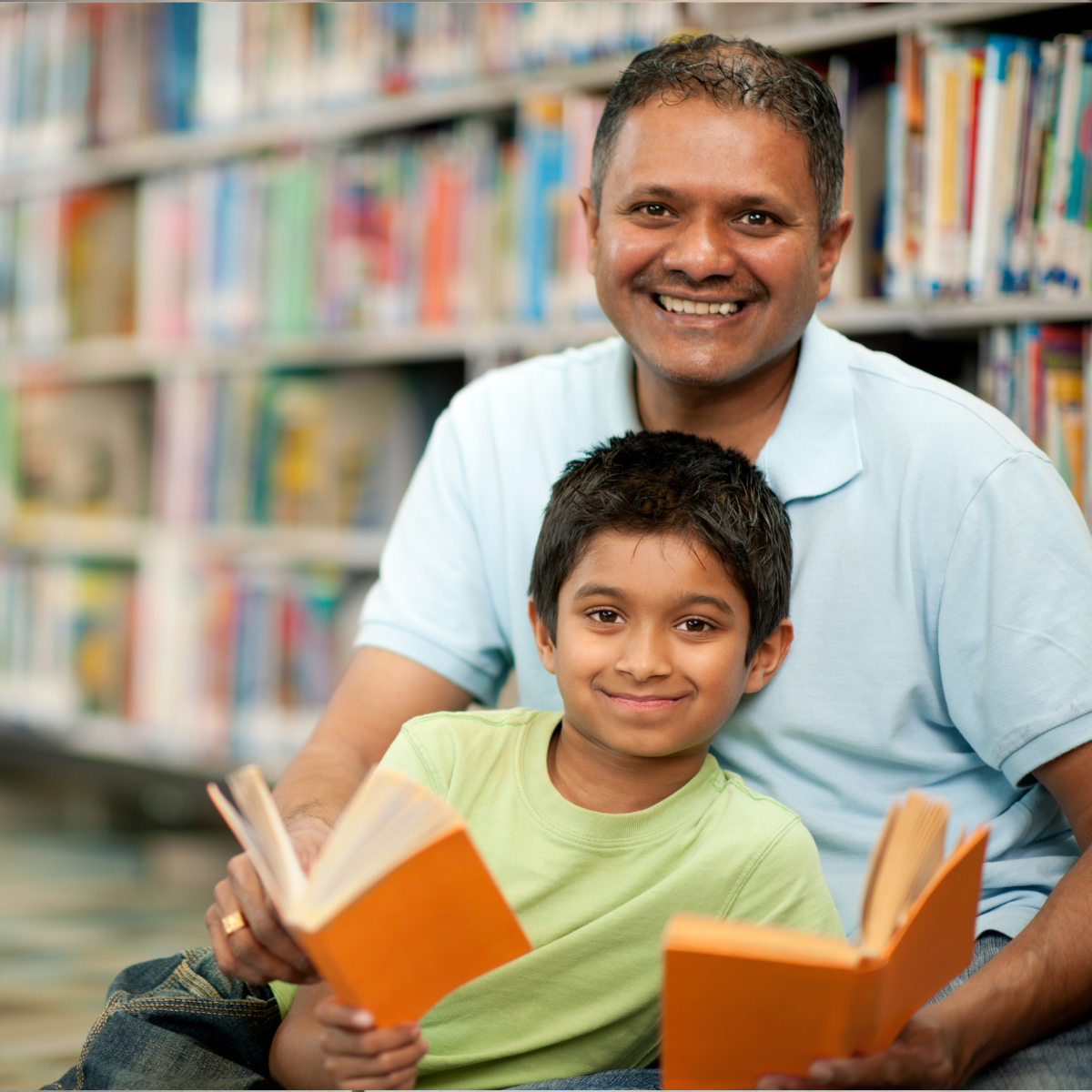 A man and a child sit together reading in a library.