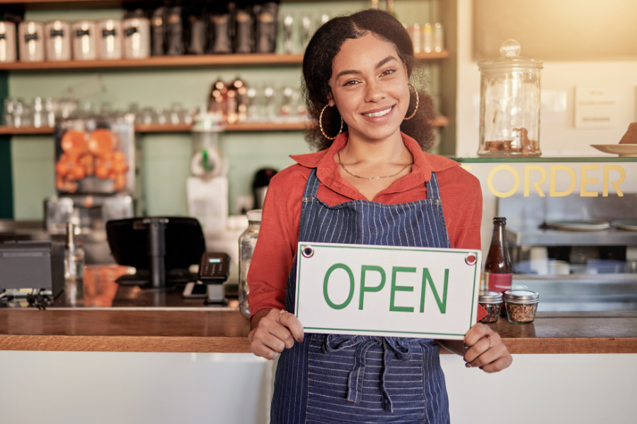 A woman holds up an open sign in front of a coffee business.