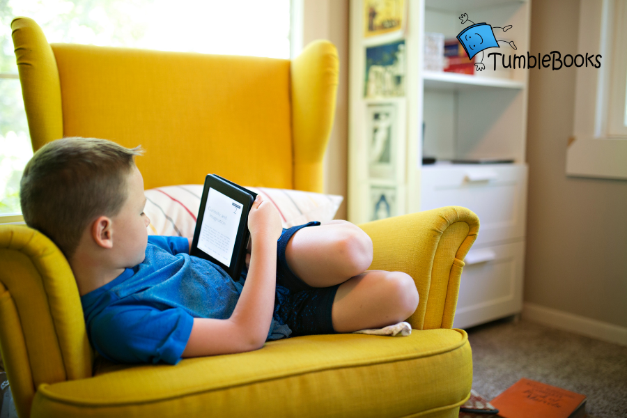A child lays in a chair reading on a tablet, points to TumbleBookLibrary.