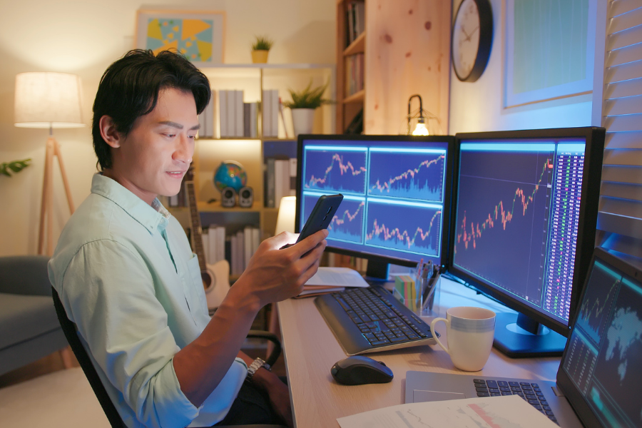 Person sits in front of computer screens with investment info while looking at phone, points to Morningstar Investment Research Center.